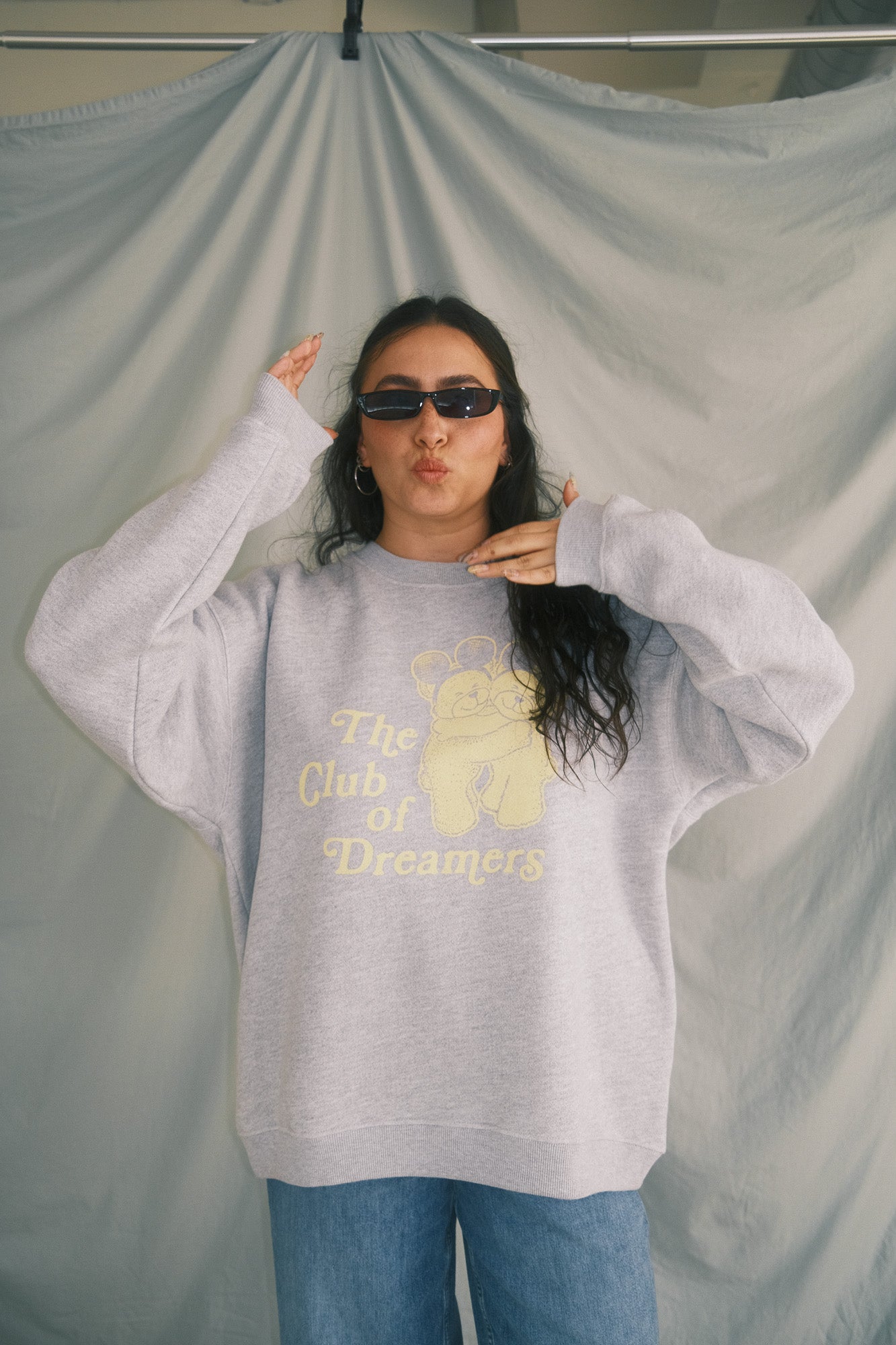 Person wearing a gray sweatshirt with a bear graphic and text, standing against a plain background.
