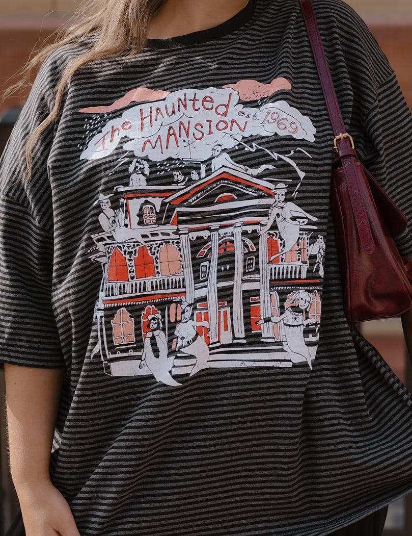 Person wearing a graphic t-shirt with 'The Haunted Mansion' design.