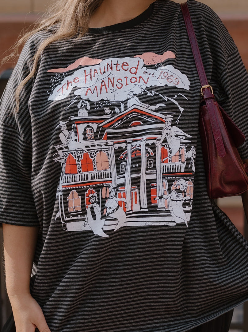 Person wearing a graphic t-shirt with 'The Haunted Mansion' design.