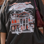 Person wearing a graphic t-shirt with 'The Haunted Mansion' design.