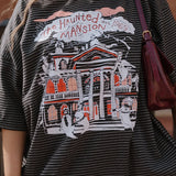 Person wearing a graphic t-shirt with 'The Haunted Mansion' design.