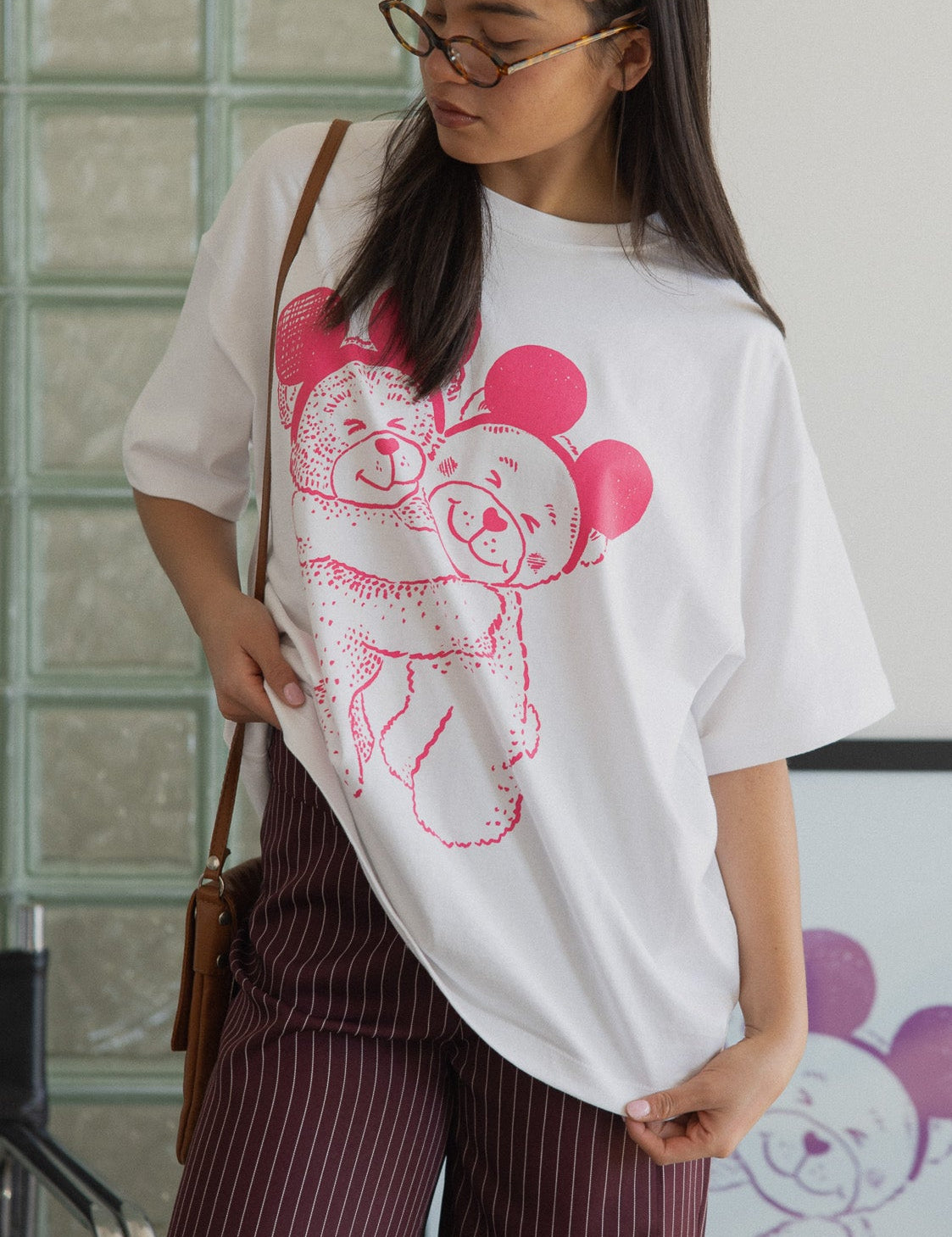 Woman wearing a white t-shirt with a pink graphic design, standing indoors.