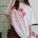 Woman wearing a white t-shirt with a pink graphic design, standing indoors.