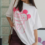 Woman wearing a white t-shirt with a pink graphic design, standing indoors.