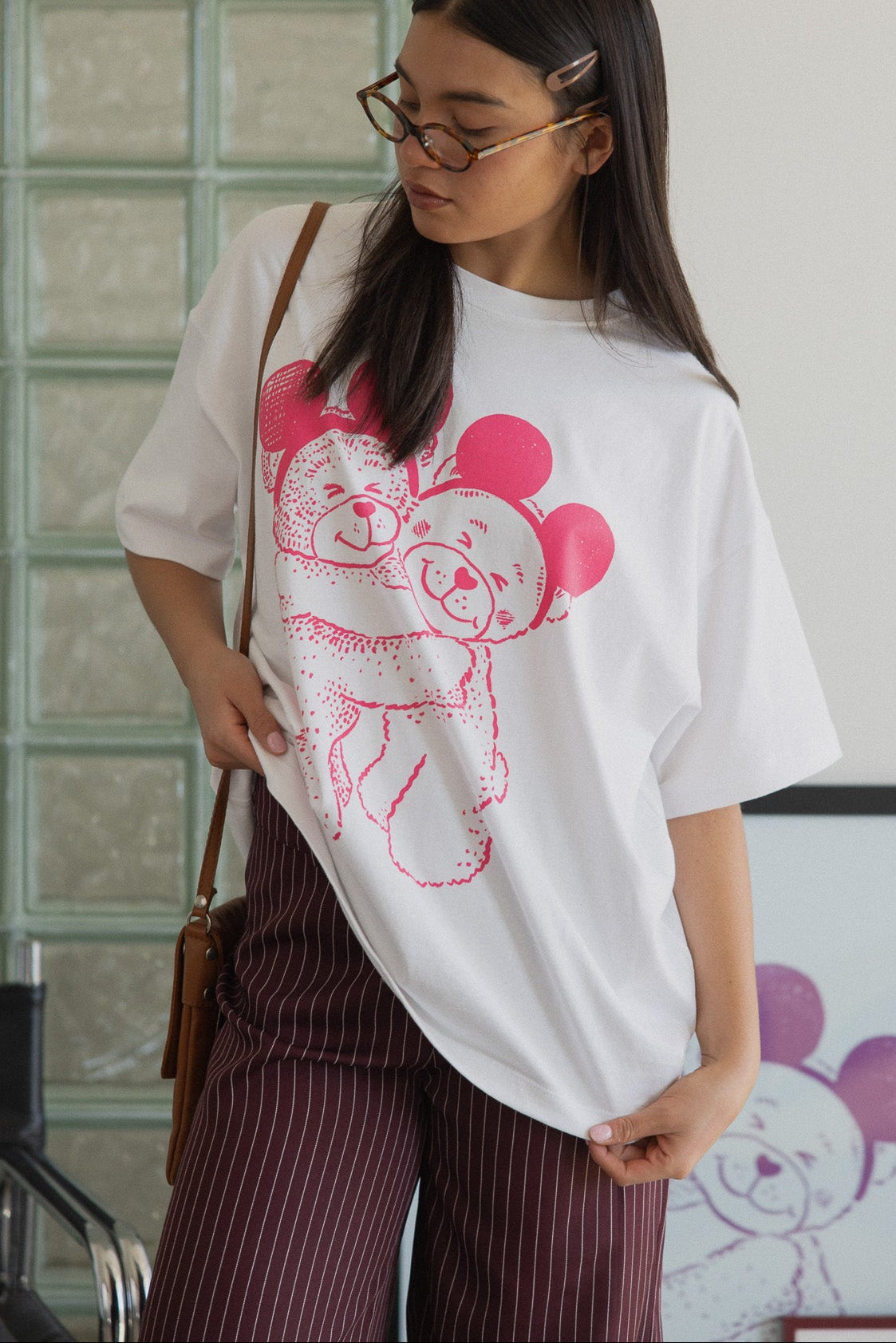 Woman wearing a white t-shirt with a pink graphic design, standing indoors.