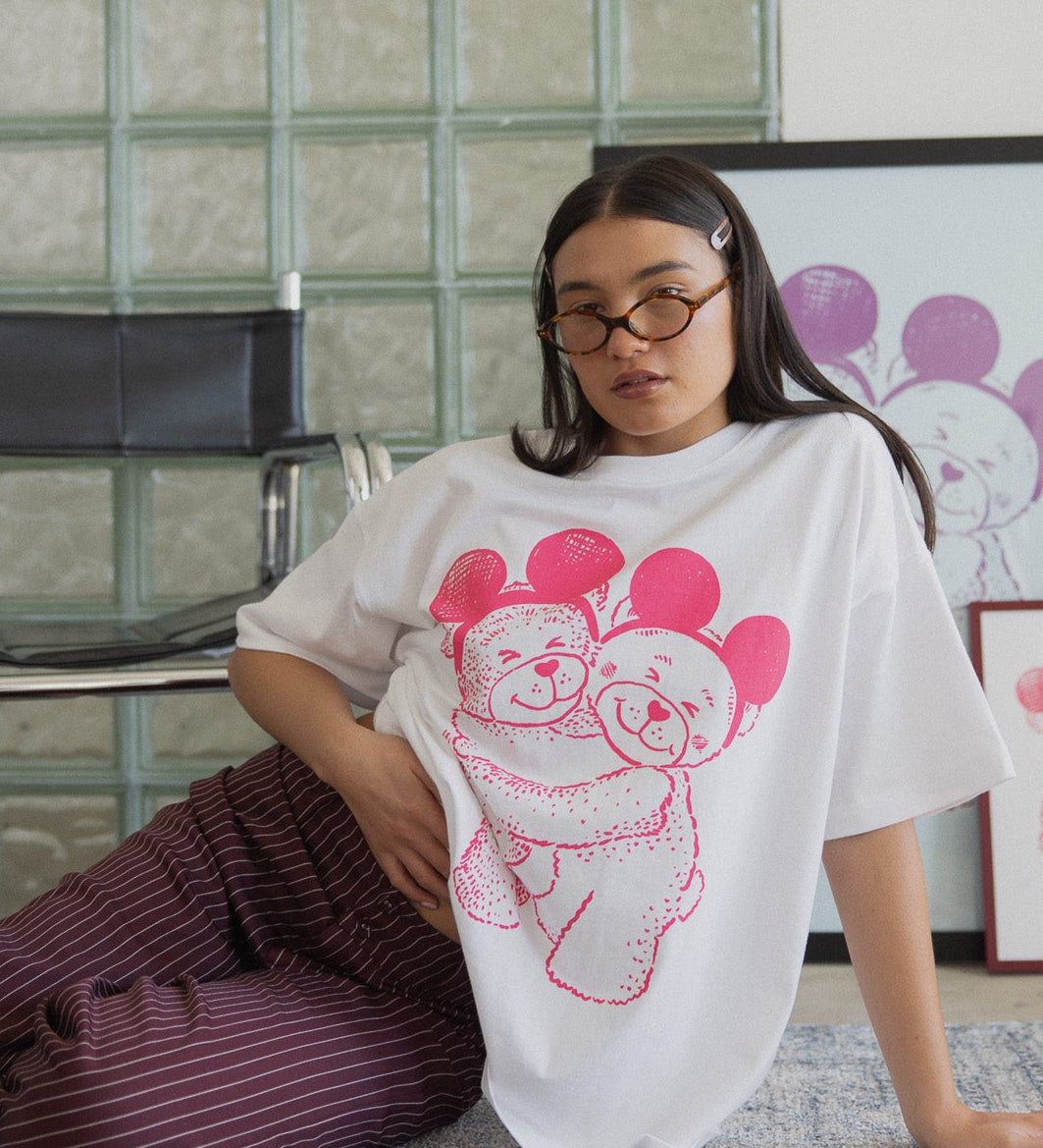 Person wearing a white t-shirt with pink graphic design sitting on the floor against a glass block wall.