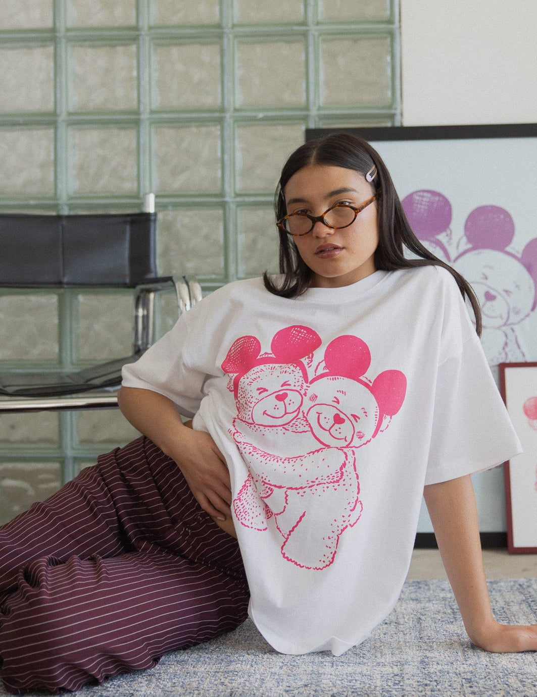 Person wearing a white t-shirt with pink graphic design sitting on the floor against a glass block wall.