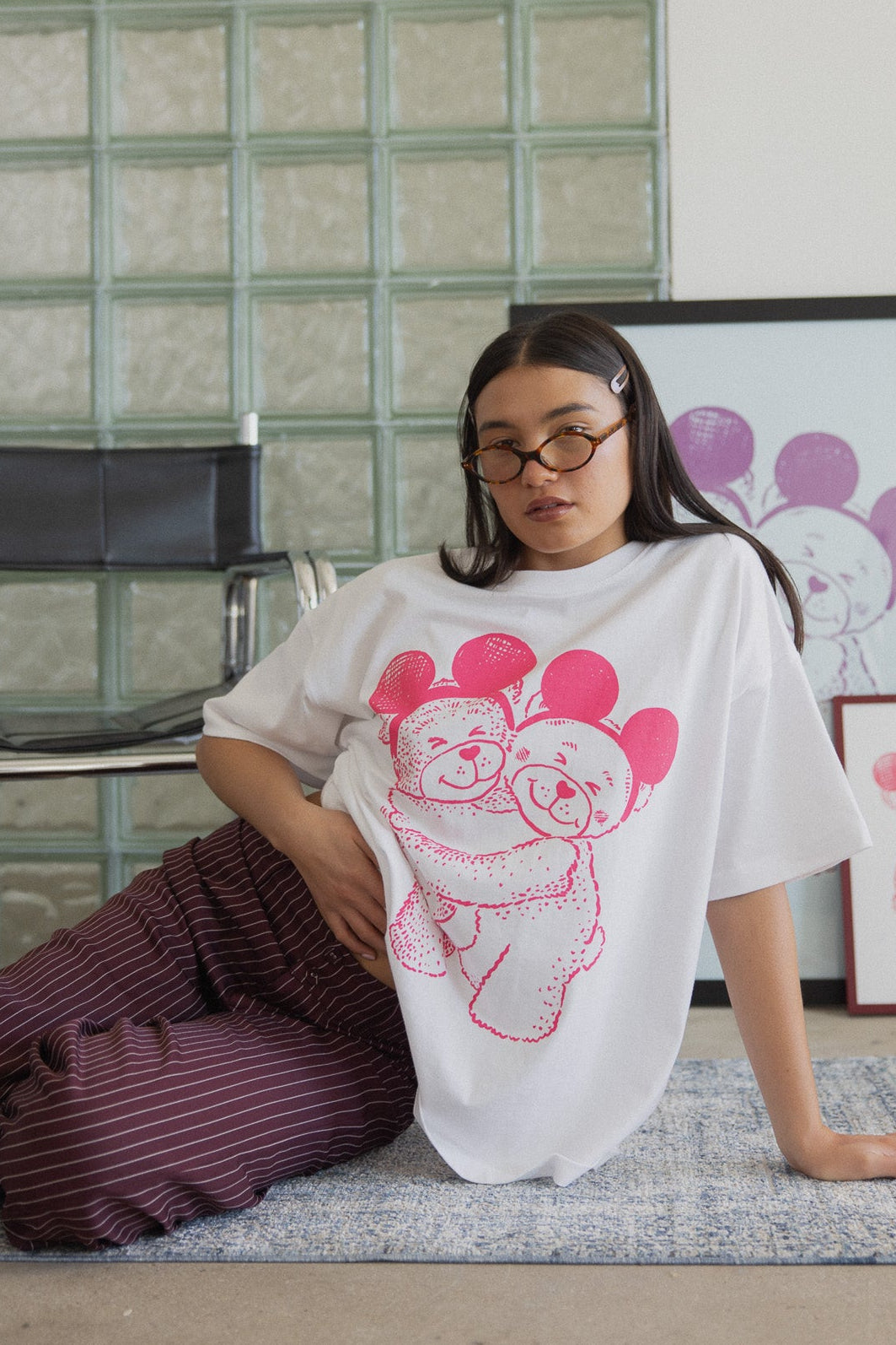 Person wearing a white t-shirt with pink graphic design sitting on the floor against a glass block wall.