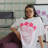 Person wearing a white t-shirt with pink graphic design sitting on the floor against a glass block wall.