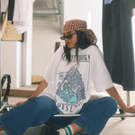Person sitting on a chair wearing a graphic t-shirt and sunglasses in a clothing store.