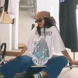 Person sitting on a chair wearing a graphic t-shirt and sunglasses in a clothing store.