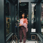 a girl standing in a black doorway with windows, holding the door open, wearing the splash mountain shirt looking at the camera