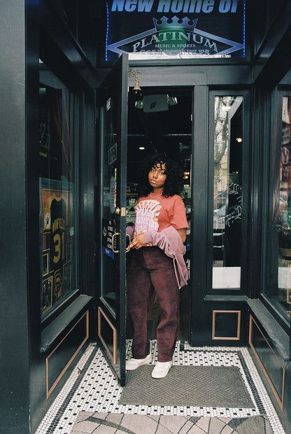 a girl standing in a black doorway with windows, holding the door open, wearing the splash mountain shirt looking at the camera